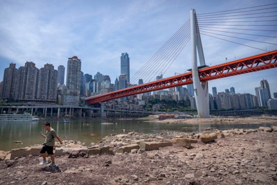 A man walks along the lower than normal bank of the Jialing River in southwestern China's Chongqing Municipality, Friday, Aug. 19, 2022. Ships crept down the middle of the Yangtze on Friday after the driest summer in six decades left one of the mightiest rivers shrunk to barely half its normal width and set off a scramble to contain damage to a weak economy in a politically sensitive year.