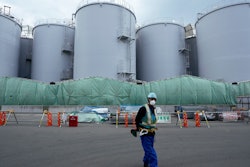 A worker helps direct a truck driver as he stands near tanks used to store treated radioactive water after it was used to cool down melted fuel at the Fukushima Daiichi nuclear power plant, run by Tokyo Electric Power Company Holdings (TEPCO), in Okuma town, northeastern Japan, on March 3, 2022.
