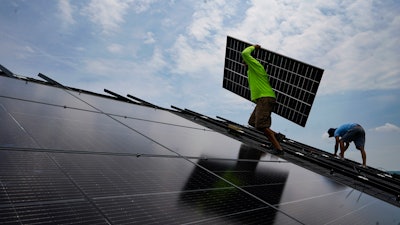 Nicholas Hartnett, owner of Pure Power Solar, carries a panel as he and Brian Hoeppner, right, install a solar array on the roof of a home in Frankfort, Ky., July 17, 2023.