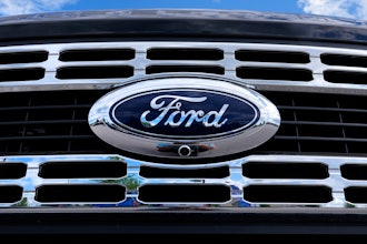 The Ford logo is shown on the grill of a pick-up truck on a dealership lot.