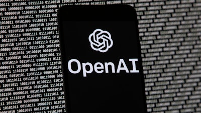 The OpenAI logo appears on a mobile phone in front of a computer screen with random binary data.