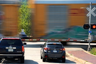 Cars wait at a railroad crossing in Homestead, Pa., as a CSX freight train rolls through.
