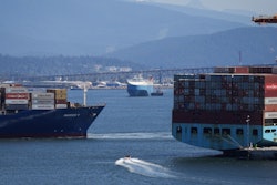 A boater passes between cargo ships on the harbor in Vancouver, British Columbia, July 16, 2024.