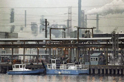 The Exxon oil refinery stands in Linden, N.J., Jan. 9, 1990, as two clean harbor cleanup boats work in the Arthur Kill waterway.