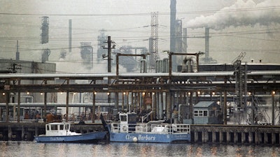 The Exxon oil refinery stands in Linden, N.J., Jan. 9, 1990, as two clean harbor cleanup boats work in the Arthur Kill waterway.