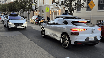 Two Waymo driverless taxis stop before passing one another on a San Francisco street on Feb. 15, 2023.