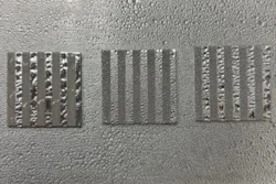 Aluminum coupon samples patterned with alternating stripes of smooth (lighter) and etched (darker) topographies display contrasting wettability.