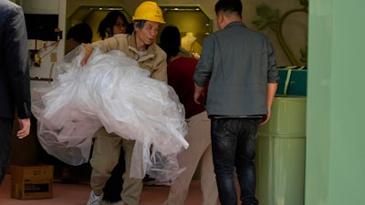 A worker removes plastic sheets after setting up a booth at a mall in Beijing, Wednesday, May 7, 2025.