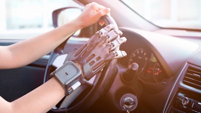 A person with a prosthetic hand printed on a 3d printer at the wheel of a car.
