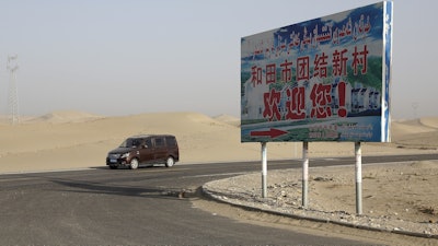 A car drives through a desert where a signboard which reads 'Welcome to the Hotan Unity New Village' is seen on display in Hotan, in western China's Xinjiang region on Sept. 21, 2018.