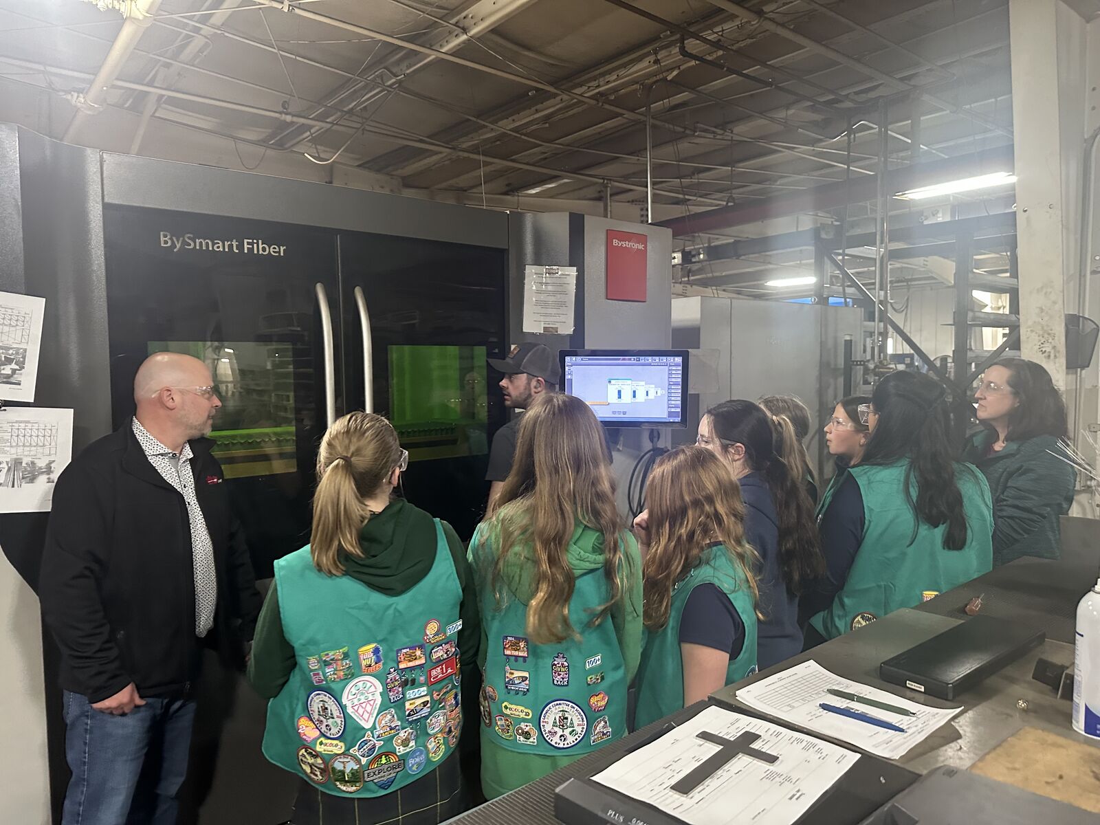 Unifab President Matt Hill (left) and Girl Scout Troop 80452 watching the signs being cut in one of Unifab’s laser cutting machines.