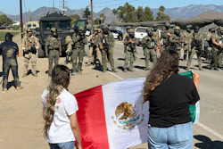Demonstrators hold a flag in front of federal agents blocking a road during an immigration raid in Camarillo, Calif.