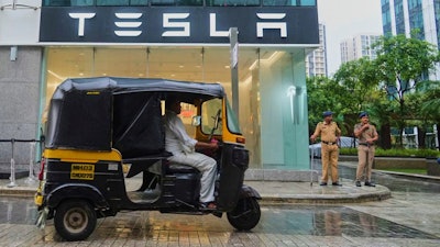 Policemen stand guard as a three-wheeler auto-rickshaw drives past India's first Tesla showroom to be inaugurated in Mumbai, India, Tuesday, July 15, 2025.