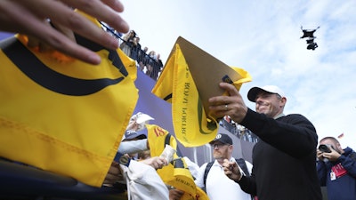Rory McIlroy of Northern Ireland signs autographs on the 18th green watched by the new Spidercam, top right, following a practice round for the British Open golf championship at the Royal Portrush Golf Club, Northern Ireland, Tuesday, July 15, 2025.