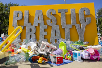 Plastic waste installation with 'PLASTIC TREATY' text on yellow background surrounded by discarded plastic items