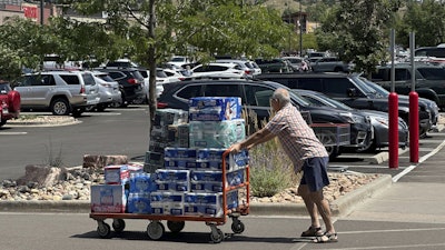 A shopper pushes a cart loaded with paper goods through the parking lot of a Costco warehouse, Aug. 12, 2025, Colorado Springs, Colo.
