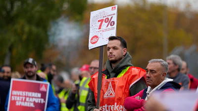 A worker holds a sign reading 'investing instead of saving' during a nationwide warning strike of the union IG Metal at the car maker FORD factory in Cologne, Germany, Germany, Oct. 29, 2024.
