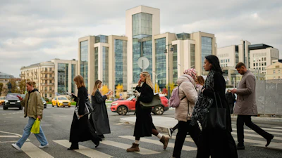 People cross a street, with Russian oil company Lukoil's headquarters seen in the background, in Moscow, Russia, Thursday, Oct. 23, 2025.