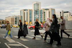People cross a street, with Russian oil company Lukoil's headquarters seen in the background, in Moscow, Russia, Thursday, Oct. 23, 2025.