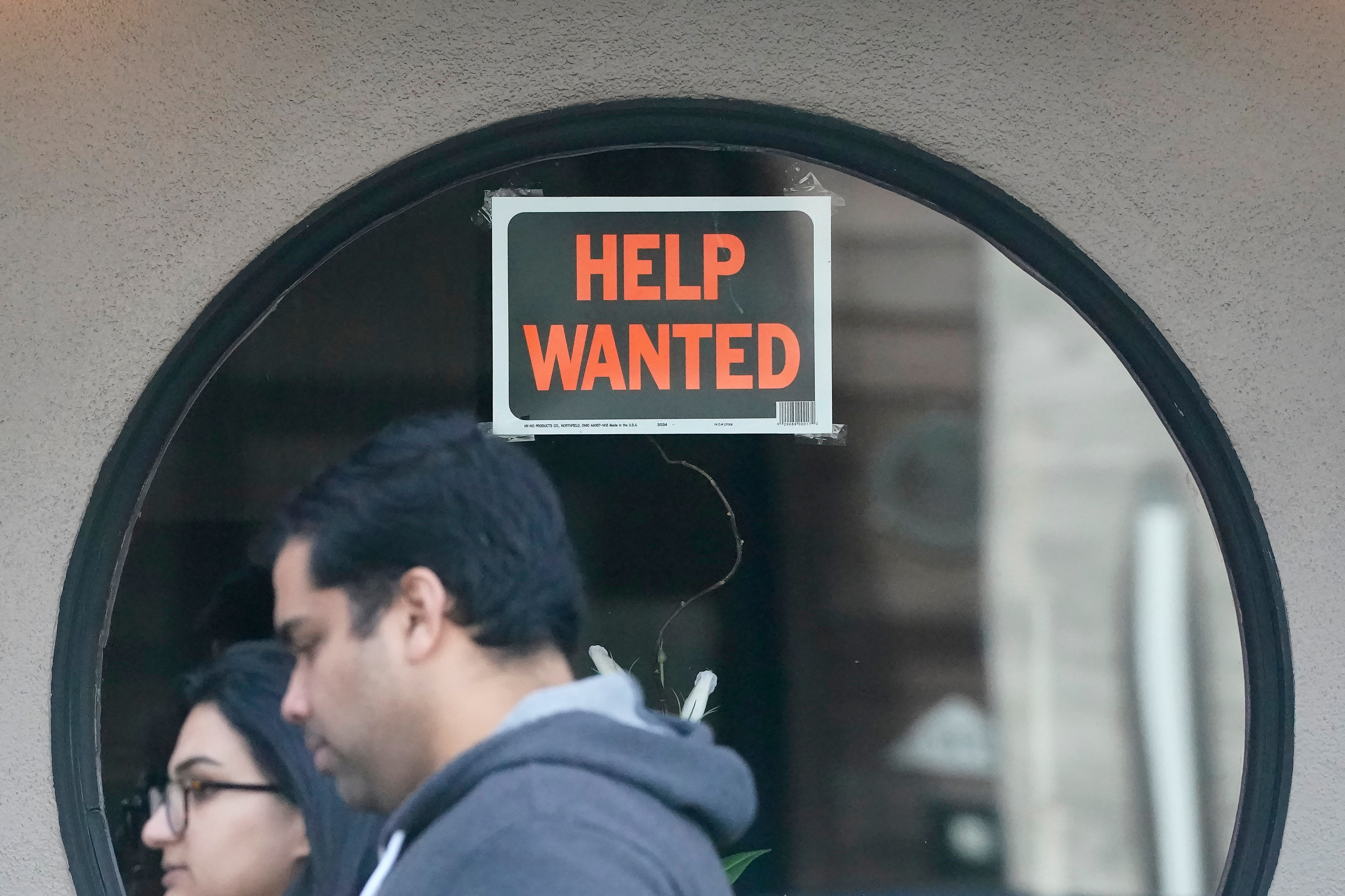 Pedestrians walk past a help wanted sign posted on the door of a restaurant in San Francisco, April 18, 2023.