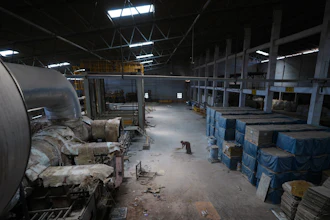 Industrial warehouse interior with machinery, storage containers, and metal framework under skylights