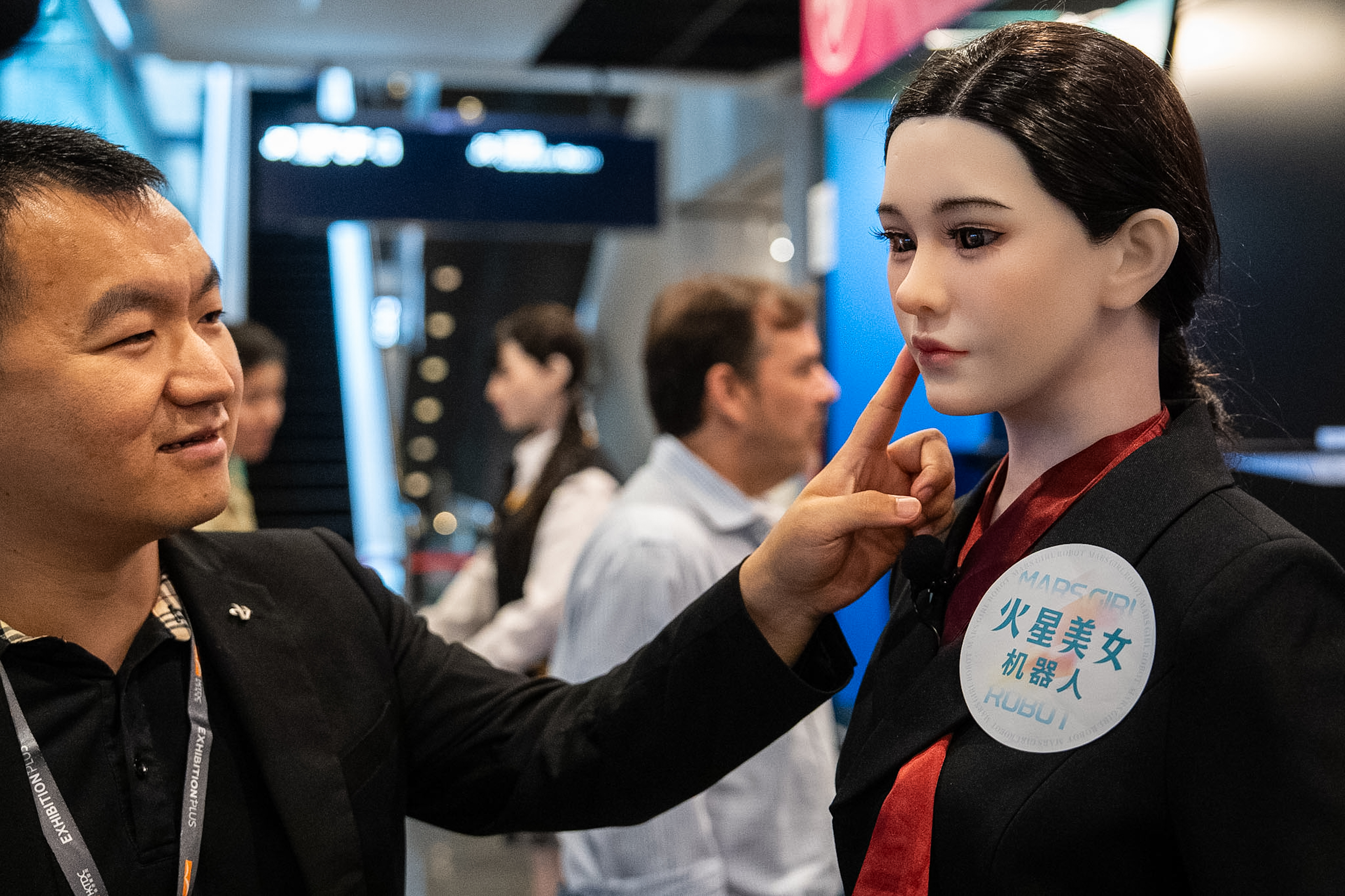 A member of staff touches the face of a humanoid robot showcased at an exhibition in Hong Kong on Monday, April 13, 2026.