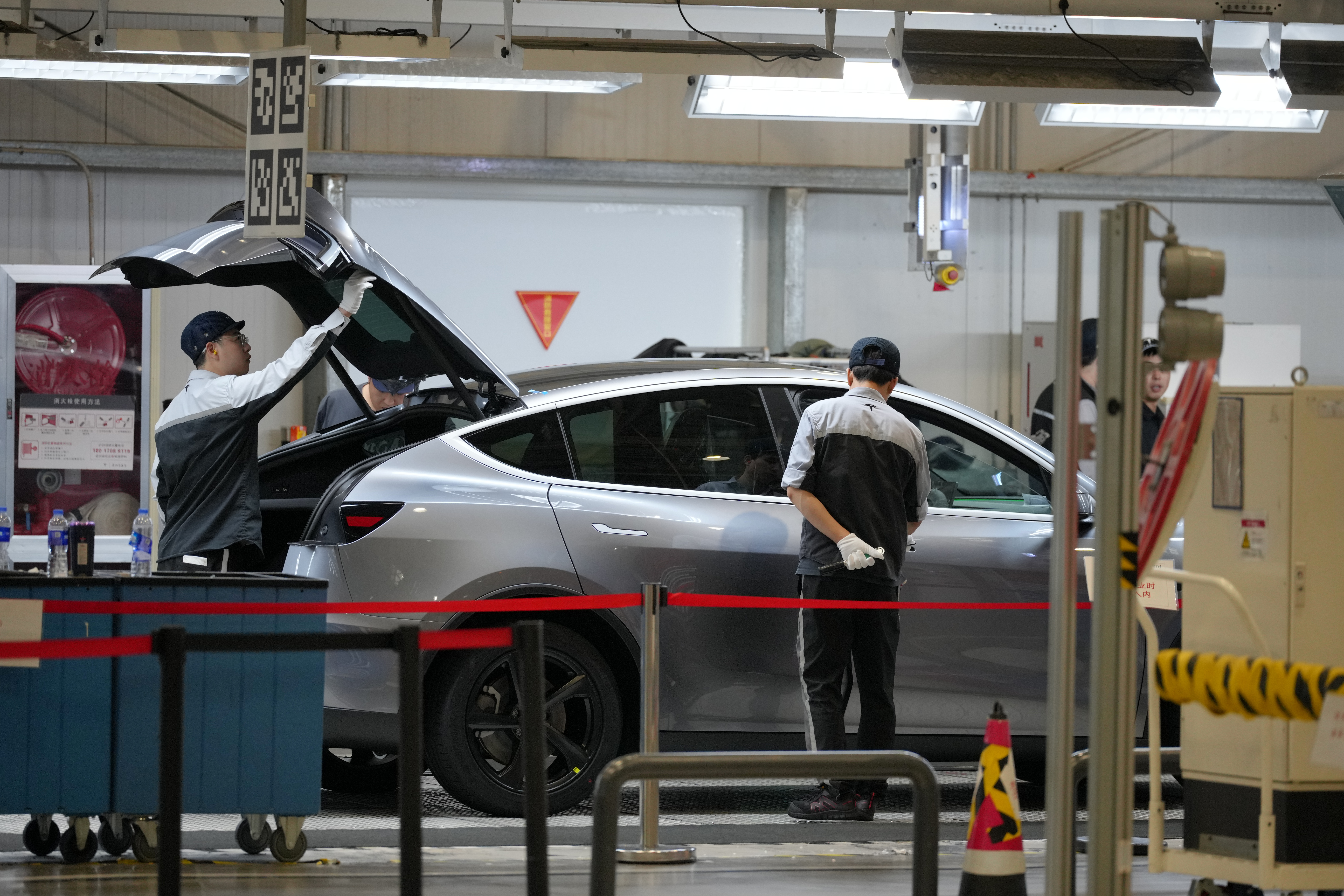 Workers check on the Tesla Model Y at the production lines at the Tesla Gigafactory assembly plant during a media organized tour, in Shanghai, China, Tuesday, April 14, 2026.