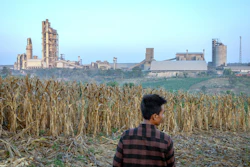 A farmer stands on a corm field as a cement factory seen in the background in Kendeng Mountains in Rembang, Central Java, Indonesia, Friday, June 19, 2026.