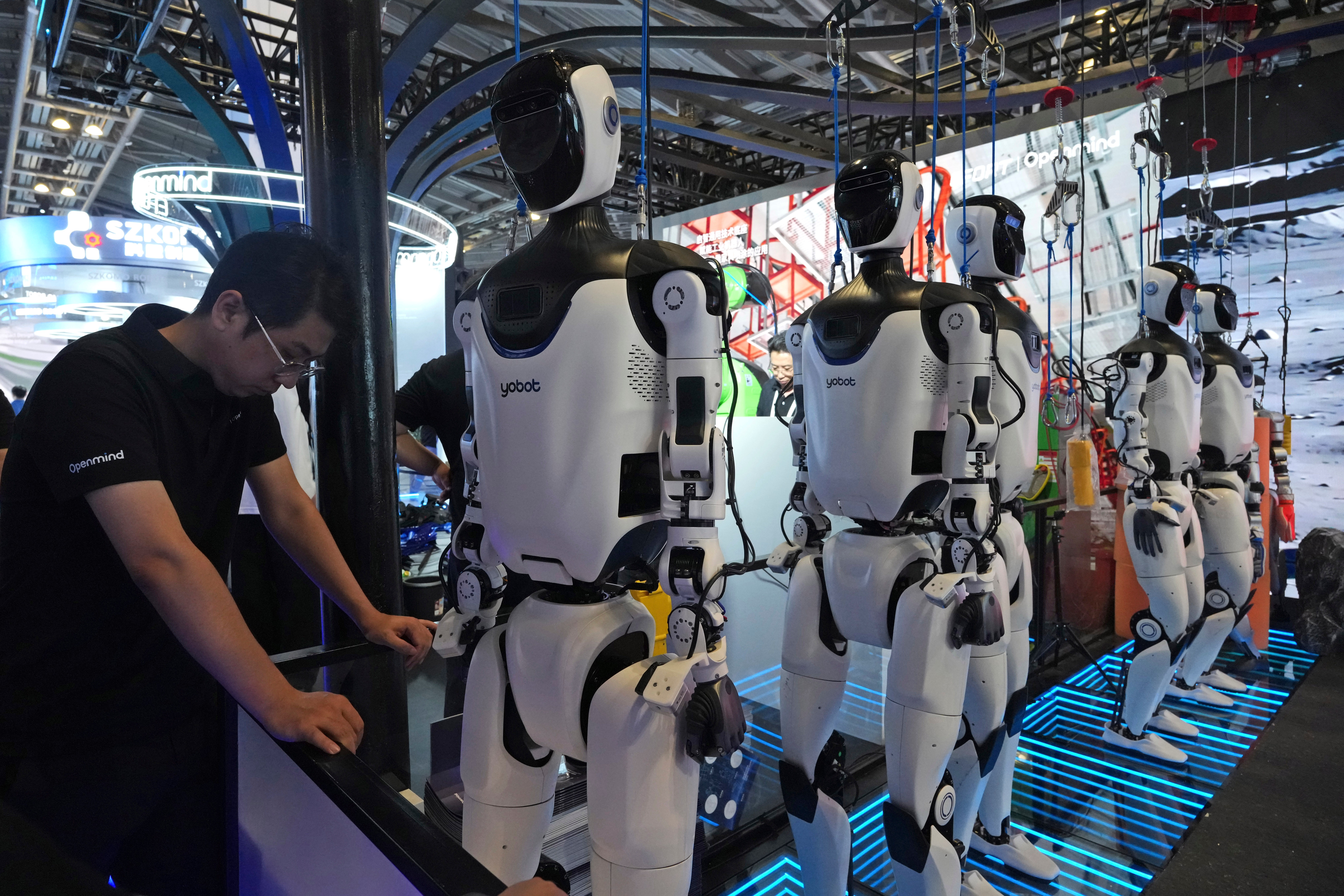 A worker reacts near a line of humanoid robots displayed at the World AI Conference in Shanghai, Friday, July 17, 2026.