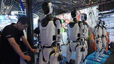 A worker reacts near a line of humanoid robots displayed at the World AI Conference in Shanghai, Friday, July 17, 2026.