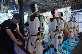A worker reacts near a line of humanoid robots displayed at the World AI Conference in Shanghai, Friday, July 17, 2026.