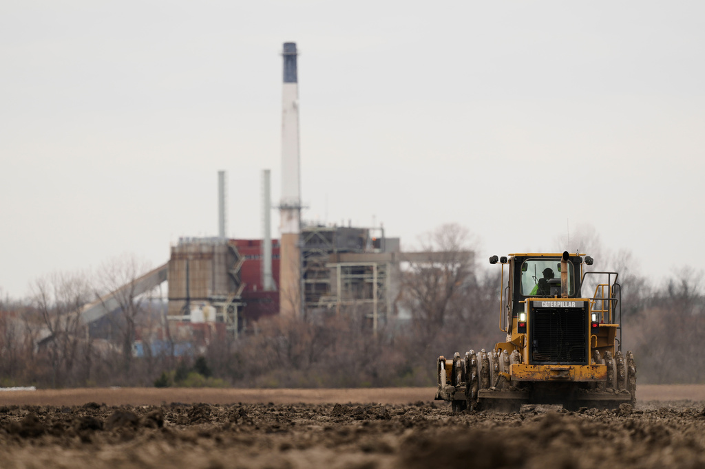 A worker prepares a plot of land for an AI data center, with a retired power plant being refurbished to provide electricity for the facility in the distance, March 24, 2026, in Independence, Mo.