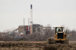 A worker prepares a plot of land for an AI data center, with a retired power plant being refurbished to provide electricity for the facility in the distance, March 24, 2026, in Independence, Mo.