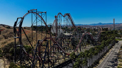 Aerial view of a steel roller coaster with red tracks winding through desert landscape and mountains in background