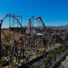 Aerial view of a steel roller coaster with red tracks winding through desert landscape and mountains in background