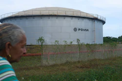 Large cylindrical PDVSA storage tank behind chain-link fence with woman in foreground