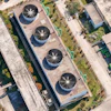 Aerial view of industrial facility with four circular cooling towers on rooftop surrounded by landscaped grounds and adjacent buildings