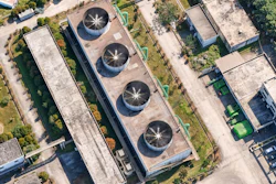 Aerial view of industrial facility with four circular cooling towers on rooftop surrounded by landscaped grounds and adjacent buildings