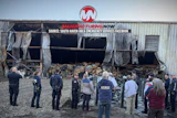 Emergency responders and firefighters assess damage at industrial warehouse with collapsed roof and debris