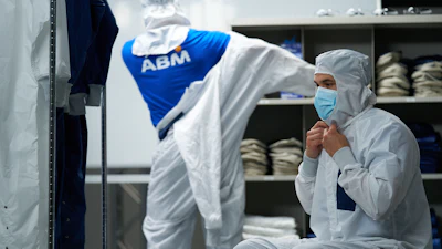 Worker in white protective suit and mask in industrial facility with shelved products and ABM branded clothing visible