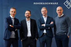 Four male professionals posing together in front of Rohde & Schwarz corporate branding backdrop