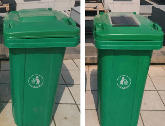 Two green recycling bins with white circular emblems on a paved outdoor surface
