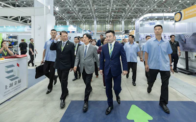 Business executives and staff tour an industrial exhibition hall with branded booths and signage