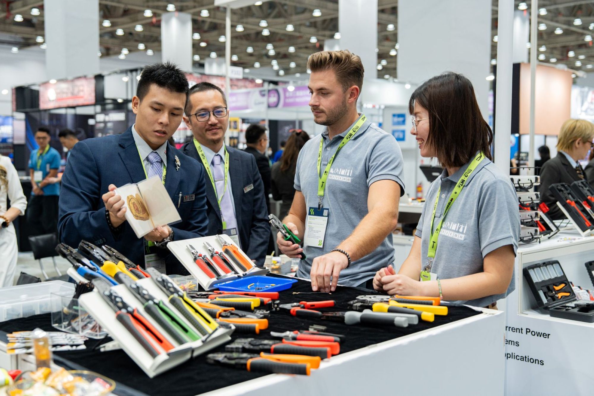 Professionals examining tools and equipment at a trade show booth with green lanyards