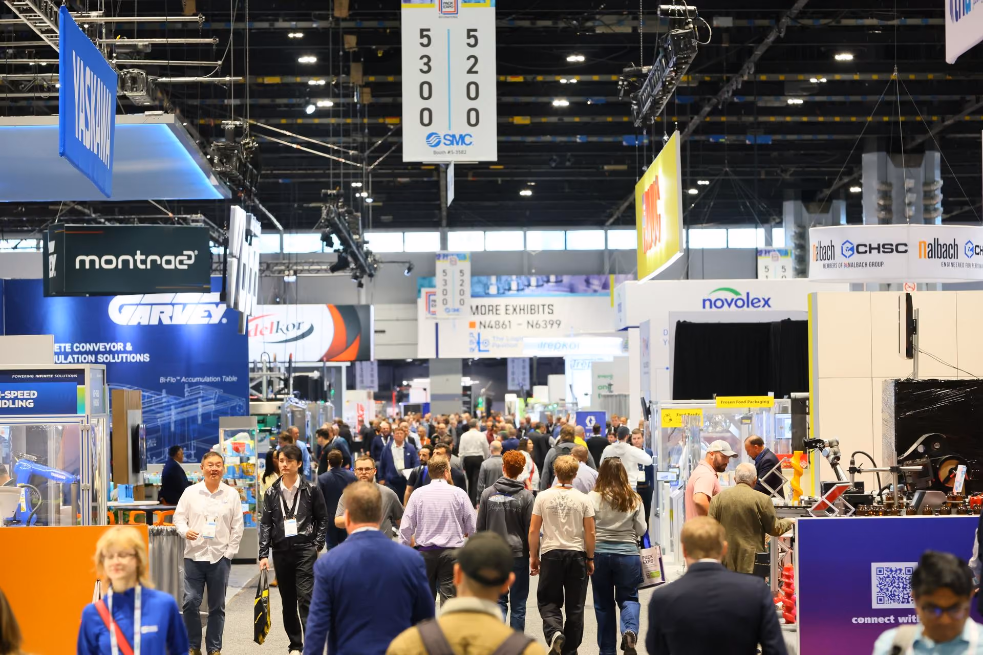Crowded trade show exhibition floor with multiple vendor booths, signage, and professional attendees networking in an indoor convention center.