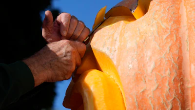 Person's hand gripping an orange and yellow metal object against a clear blue sky