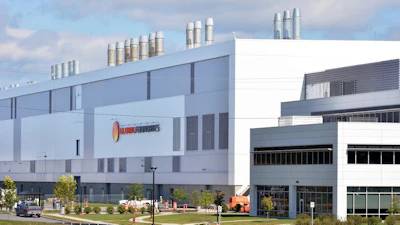 Modern industrial facility with Helios Technologies signage, featuring blue and white architecture with cylindrical ventilation stacks on the roofline.