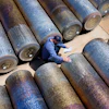 Worker in blue surveying large industrial metal pipes arranged on sandy ground from above