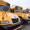 Row of yellow school buses parked in a line with bare trees in background