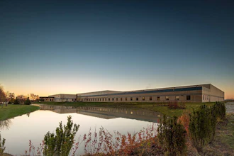 Modern industrial building complex reflected in calm water at dusk with autumn vegetation in foreground